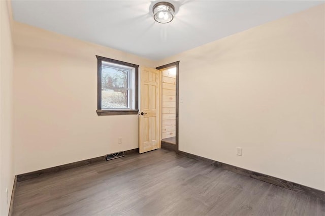 empty room featuring wood finished floors, baseboards, and visible vents