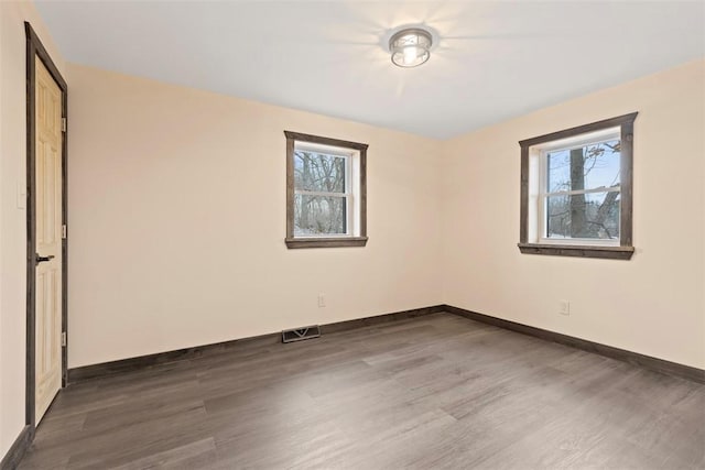 spare room featuring dark wood-type flooring, baseboards, visible vents, and a wealth of natural light