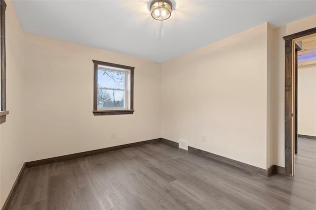 unfurnished room with dark wood finished floors, visible vents, and baseboards