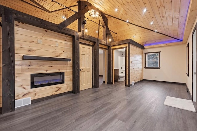 unfurnished living room with visible vents, wood walls, wood ceiling, a glass covered fireplace, and dark wood-style flooring