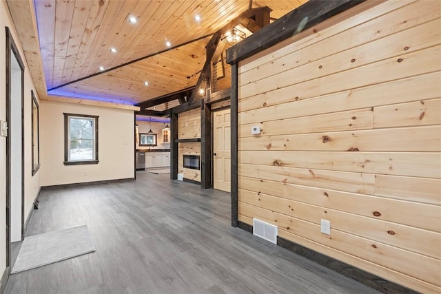 unfurnished room with visible vents, a glass covered fireplace, wooden walls, wooden ceiling, and dark wood-style flooring