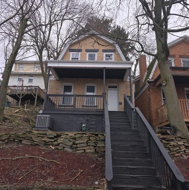 view of front facade with a gambrel roof, stairway, covered porch, central air condition unit, and brick siding