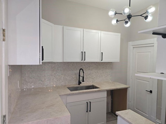 kitchen featuring backsplash, decorative light fixtures, a sink, white cabinetry, and a notable chandelier