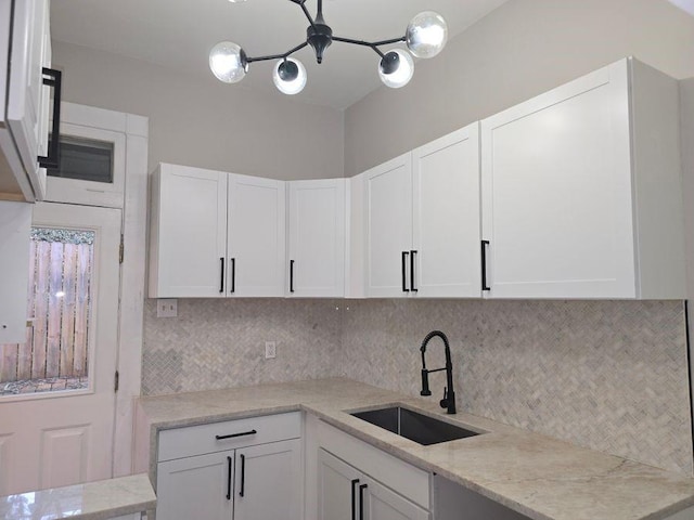 kitchen with light stone counters, white cabinetry, a sink, and decorative backsplash