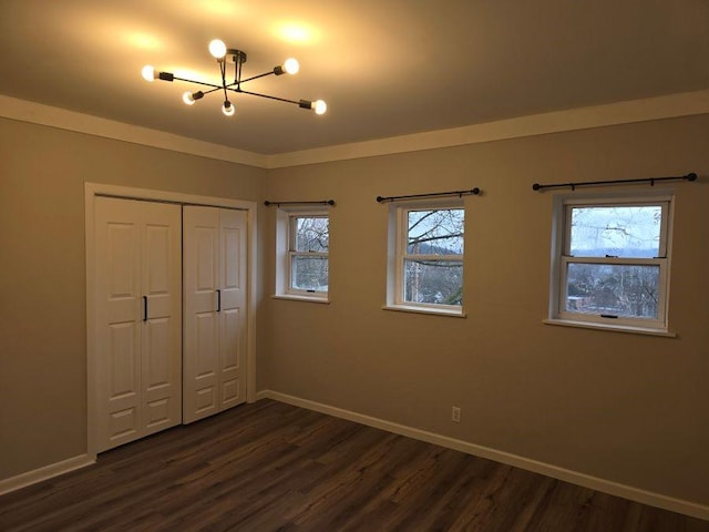 unfurnished bedroom featuring crown molding, baseboards, dark wood-style flooring, and a closet