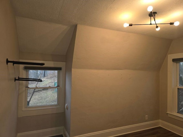 additional living space with lofted ceiling, baseboards, dark wood-type flooring, and a textured ceiling