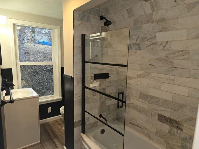 bathroom with toilet, bath / shower combo with glass door, wood finished floors, vanity, and baseboards