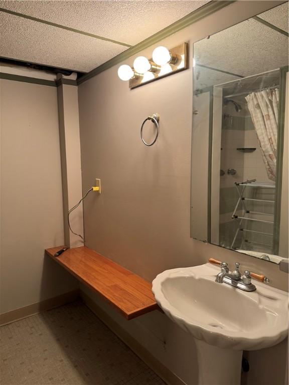 bathroom featuring baseboards, tile patterned floors, curtained shower, a textured ceiling, and a sink