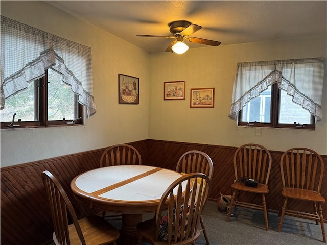 dining area featuring a ceiling fan, carpet, a wainscoted wall, and wood walls