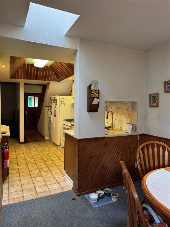 kitchen featuring range with gas cooktop, wainscoting, light carpet, and light tile patterned floors