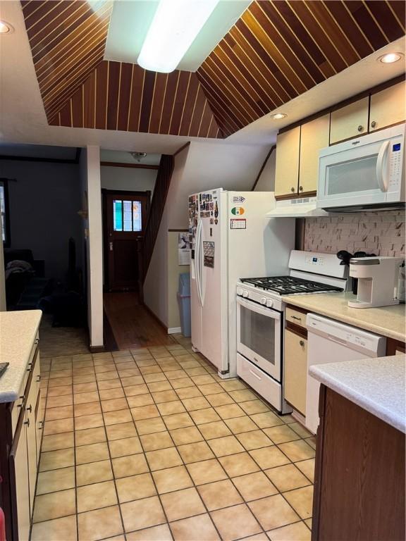 kitchen featuring light countertops, light tile patterned flooring, vaulted ceiling, white appliances, and under cabinet range hood