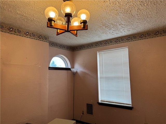 unfurnished room featuring a textured ceiling, a textured wall, a chandelier, and visible vents