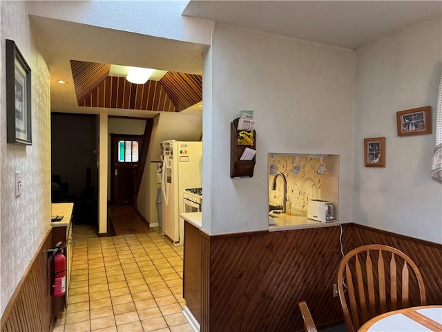 kitchen with a wainscoted wall, light countertops, light tile patterned flooring, wooden walls, and white fridge with ice dispenser