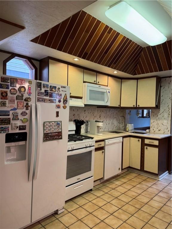 kitchen featuring light countertops, vaulted ceiling, a sink, white appliances, and under cabinet range hood