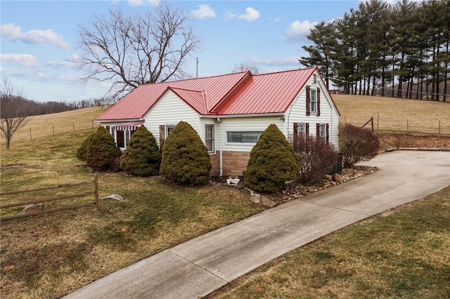 view of side of property featuring a lawn, a standing seam roof, metal roof, fence, and stone siding