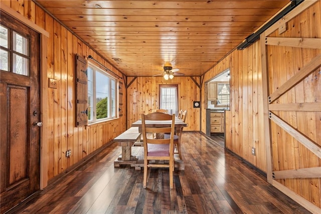 dining area with wood ceiling, wooden walls, dark wood finished floors, and a barn door