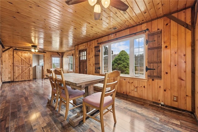 dining room with wood-type flooring, visible vents, a barn door, wooden walls, and wooden ceiling