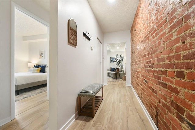 hall with light wood-type flooring, baseboards, a textured ceiling, and brick wall