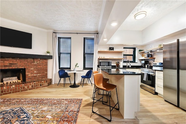 kitchen with open shelves, stainless steel appliances, dark countertops, light wood-type flooring, and a kitchen breakfast bar