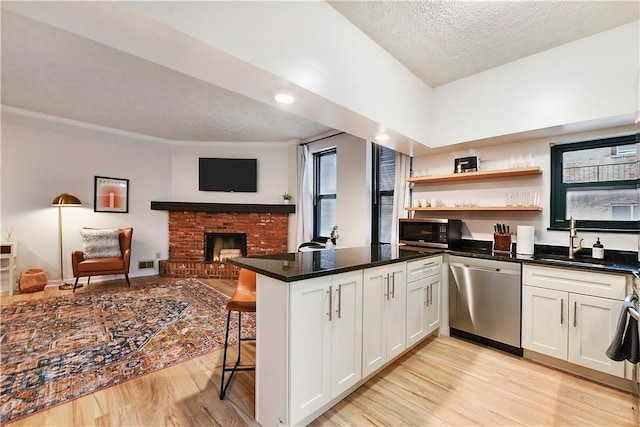 kitchen featuring light wood-style flooring, appliances with stainless steel finishes, a breakfast bar, a peninsula, and a sink