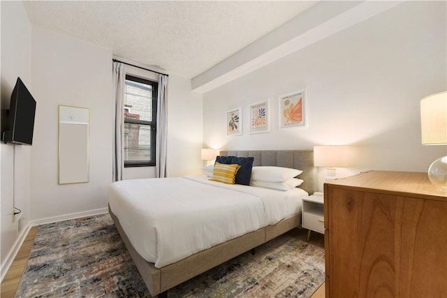 bedroom with a textured ceiling, wood finished floors, and baseboards