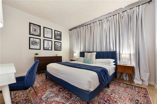 bedroom with a textured ceiling, baseboards, and wood finished floors