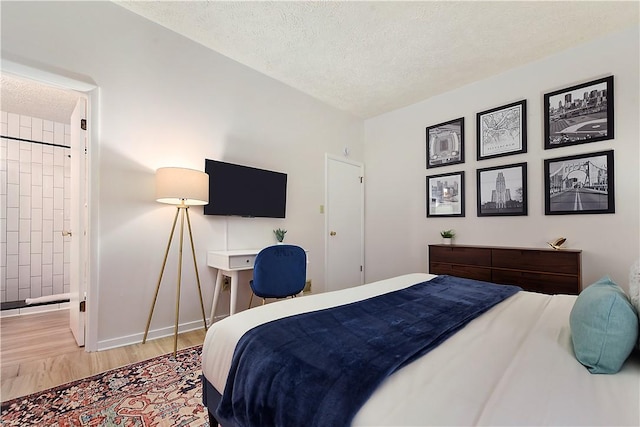 bedroom featuring a textured ceiling, light wood-type flooring, baseboards, and ensuite bathroom