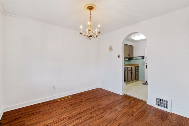 spare room featuring arched walkways, visible vents, crown molding, and wood finished floors