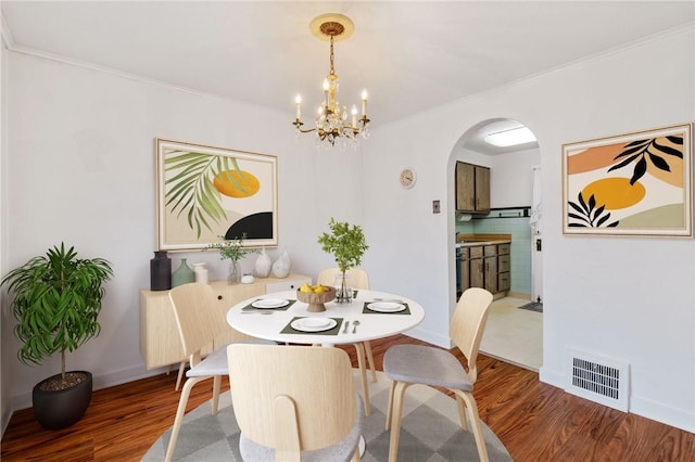 dining area featuring arched walkways, wood finished floors, visible vents, baseboards, and crown molding