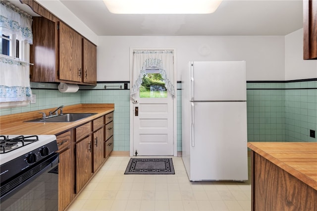 kitchen featuring black range with gas cooktop, a sink, tile walls, wainscoting, and freestanding refrigerator