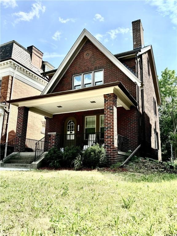 view of front of house with brick siding, a chimney, a porch, and a front yard