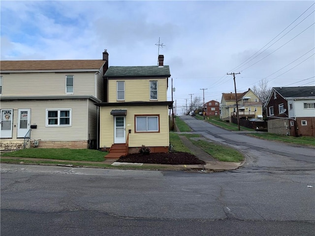 view of front facade with entry steps, a chimney, a residential view, and aphalt driveway