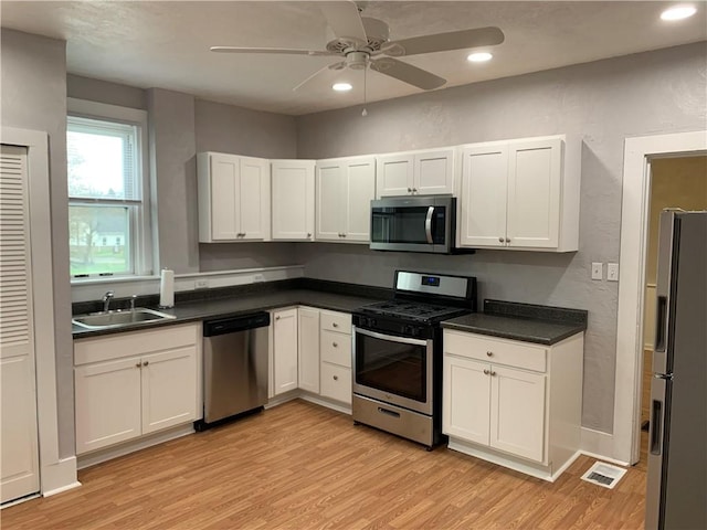 kitchen with light wood-type flooring, appliances with stainless steel finishes, white cabinets, and a sink