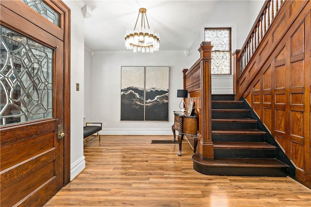 foyer entrance with a notable chandelier, crown molding, light wood-style floors, baseboards, and stairs