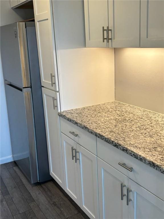 kitchen featuring light stone countertops, dark wood finished floors, white cabinets, and freestanding refrigerator