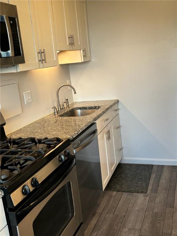 kitchen featuring light stone countertops, dark wood-style floors, white cabinets, stainless steel appliances, and a sink