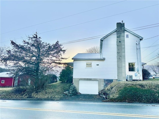 view of side of home with metal roof, a chimney, an attached garage, and central air condition unit