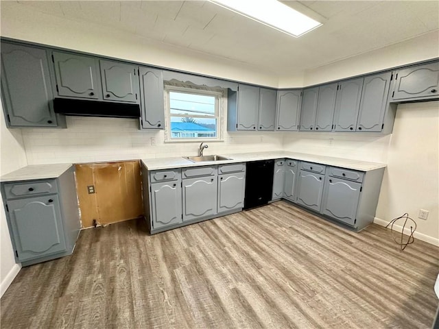 kitchen with under cabinet range hood, light wood finished floors, a sink, and gray cabinetry