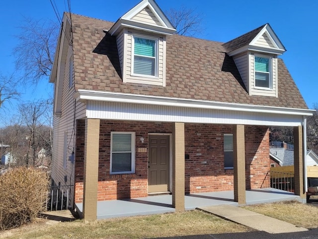 view of front of house featuring a shingled roof, a porch, and brick siding