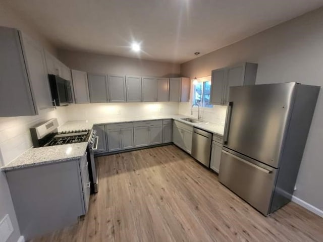 kitchen featuring light wood-style floors, stainless steel appliances, a sink, and gray cabinetry