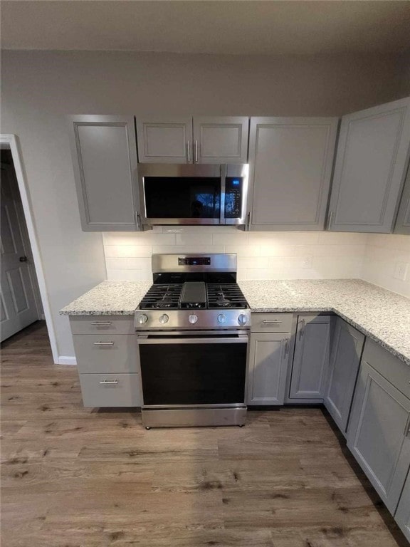 kitchen with appliances with stainless steel finishes, light wood-type flooring, gray cabinets, and tasteful backsplash