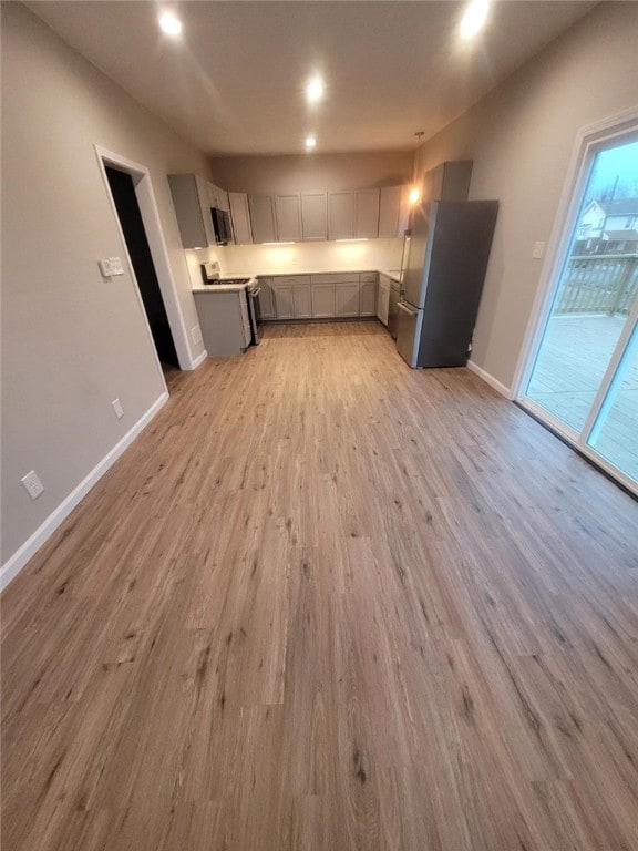 kitchen featuring light wood-style flooring, gray cabinetry, freestanding refrigerator, gas range, and baseboards