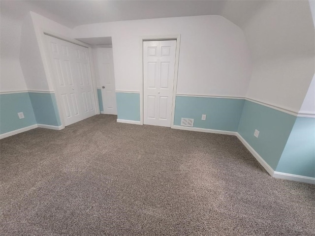 unfurnished bedroom with carpet, visible vents, vaulted ceiling, and baseboards