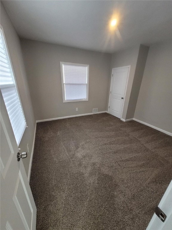 unfurnished room with dark colored carpet and baseboards