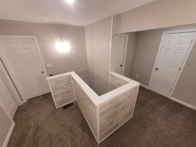 corridor with dark colored carpet, baseboards, and an upstairs landing