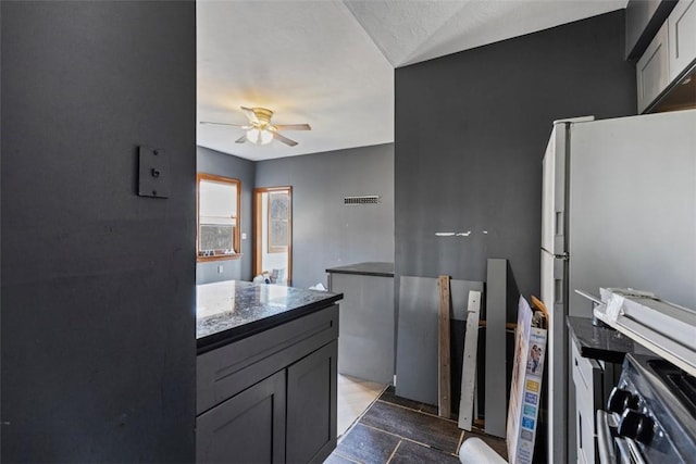 kitchen with ceiling fan, dark stone countertops, and freestanding refrigerator