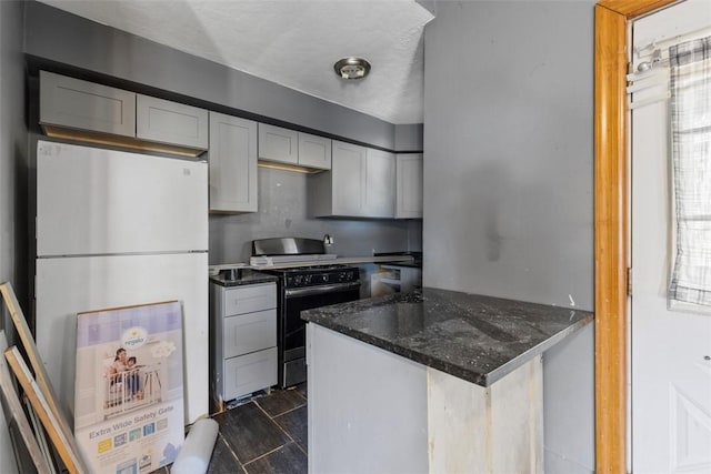 kitchen featuring a peninsula, white cabinets, freestanding refrigerator, dark stone counters, and black gas range oven