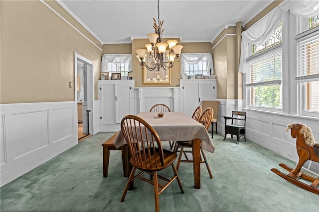 carpeted dining area featuring a wainscoted wall, ornamental molding, a decorative wall, and a notable chandelier