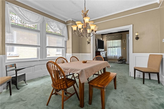 dining space with a wainscoted wall, crown molding, a decorative wall, light carpet, and a chandelier