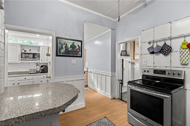 kitchen featuring a wainscoted wall, light wood-style flooring, appliances with stainless steel finishes, ornamental molding, and white cabinets